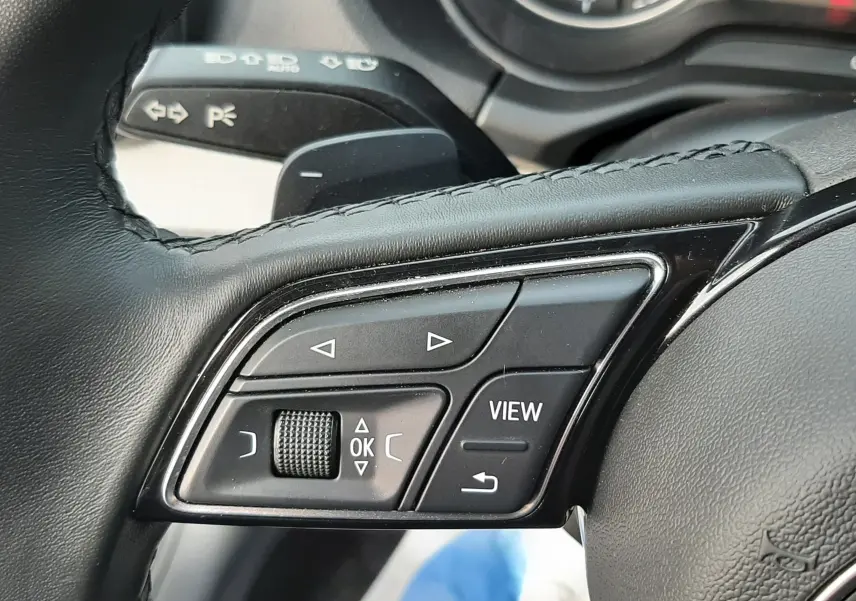 Gros plan sur les commandes au volant en cuir noir de l'Audi Q2 35 TFSI S-Line 2023, avec tableau de bord en arrière-plan.