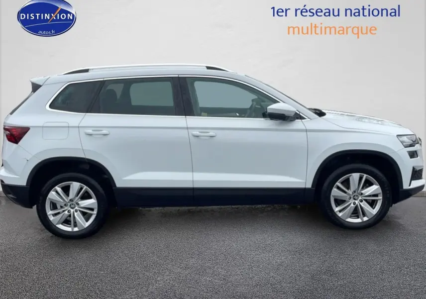 Vue de profil côté gauche d'un Skoda Karoq blanc glacial avec jantes alliage et barres de toit noires.
