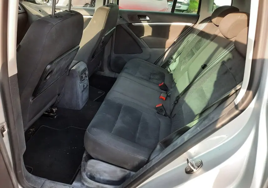 Vue intérieure arrière côté droit du Volkswagen Tiguan gris argent 2012, sièges arrière en tissu noir avec ceintures visibles.