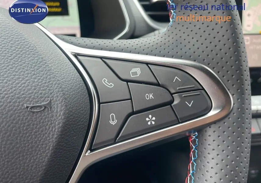 Gros plan sur les commandes au volant perforé avec surpiqûres tricolores du Renault Captur E-Tech hybride 2025 bleu iron metal.