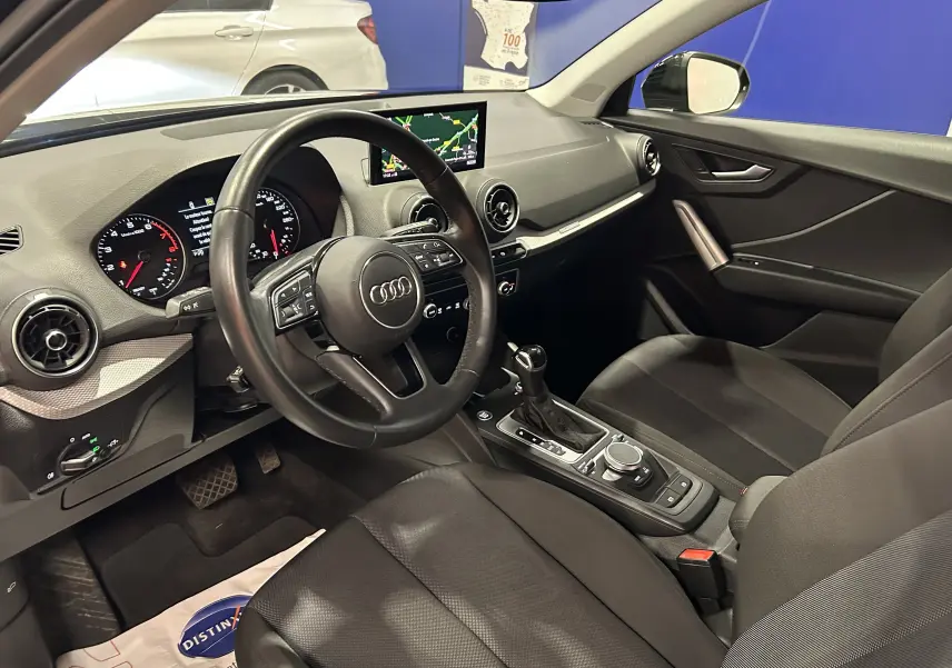 Intérieur de l'Audi Q2 35 TFSI 2023 vu côté conducteur, avec tableau de bord noir et écran GPS central.