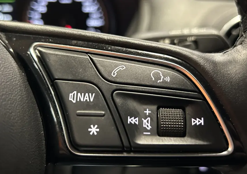 Gros plan sur les commandes du volant à gauche de l'Audi Q2 2023 noir métal, avec boutons directionnels et fonction View.