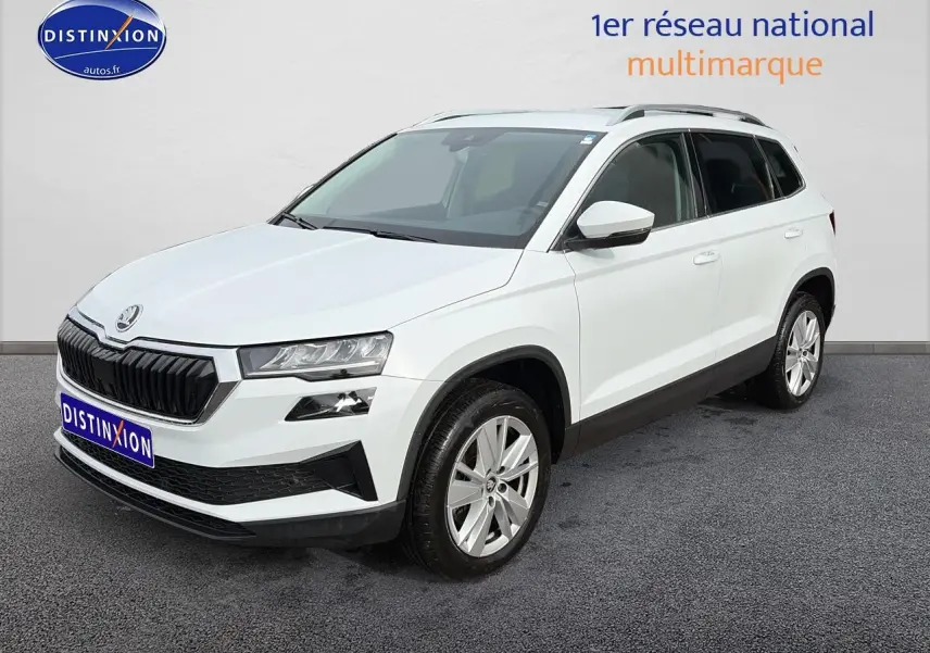 Vue 3/4 avant d'un Skoda Karoq blanc glacial avec jantes alu et barres de toit noires sur fond neutre.