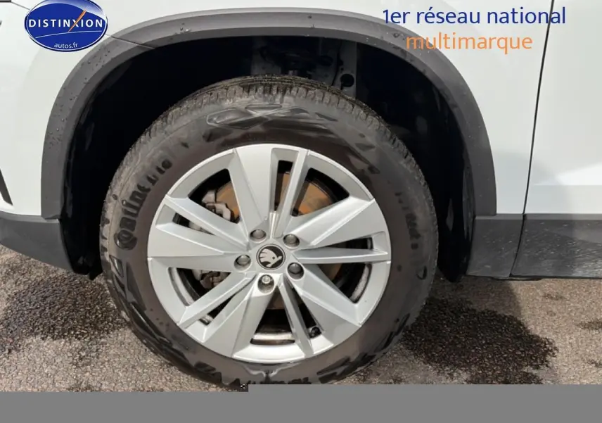 Gros plan sur la roue avant gauche d'un Skoda Karoq blanc glacial avec jante alu et logo Skoda au centre.