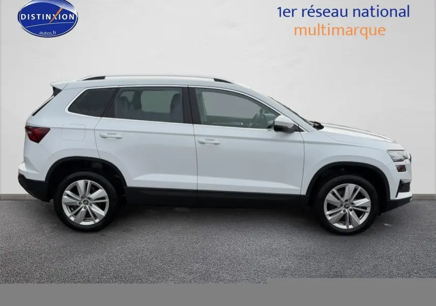 Vue latérale droite d'un Skoda Karoq blanc glacial avec jantes alliage et barres de toit noires.