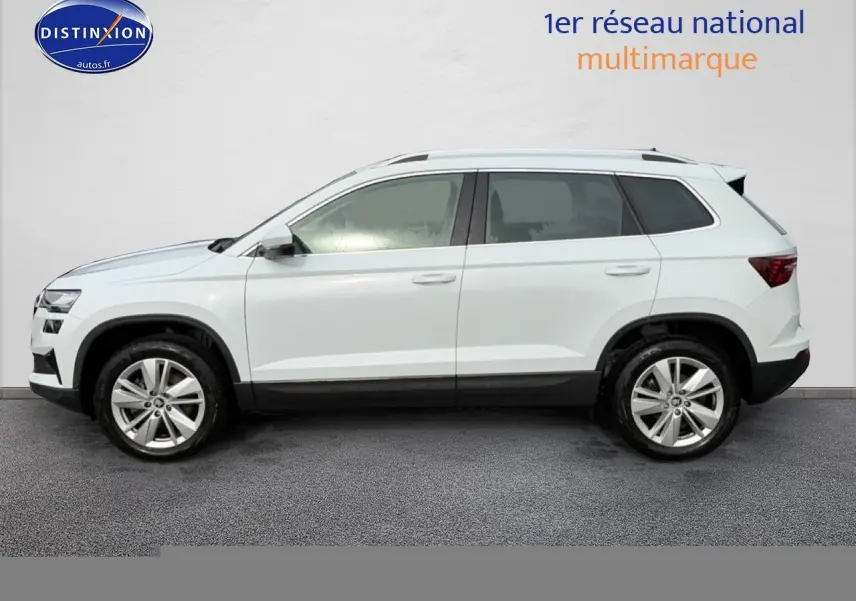 Vue latérale droite d'un Skoda Karoq blanc glacial avec jantes alu et barres de toit visibles.