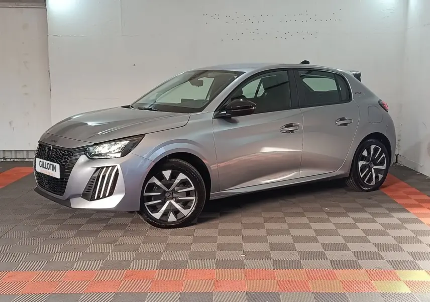 Peugeot 208 Hybrid gris clair vue de profil droit en intérieur, avec jantes stylisées et phares LED allumés.