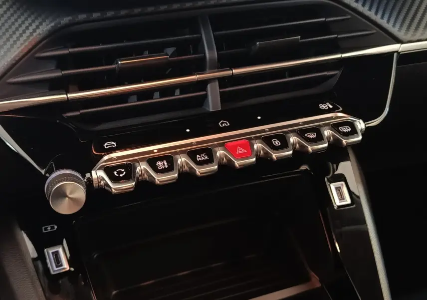 Gros plan sur la console centrale noire de la Peugeot 208 Hybrid 2025 avec boutons argentés et rouge d’alerte.