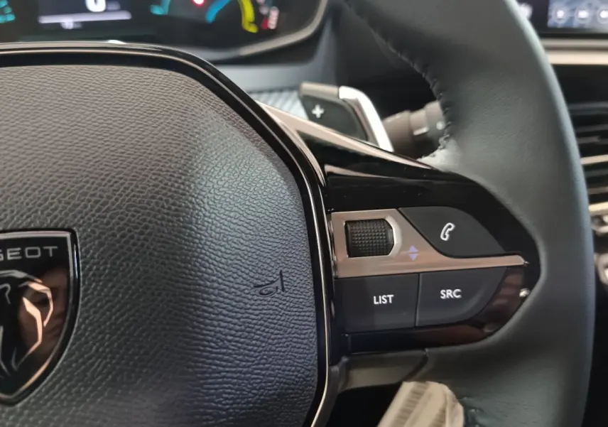 Gros plan sur le volant cuir noir de la Peugeot 208 Hybrid 100 e-DCS6 Style, avec commandes multifonctions visibles.