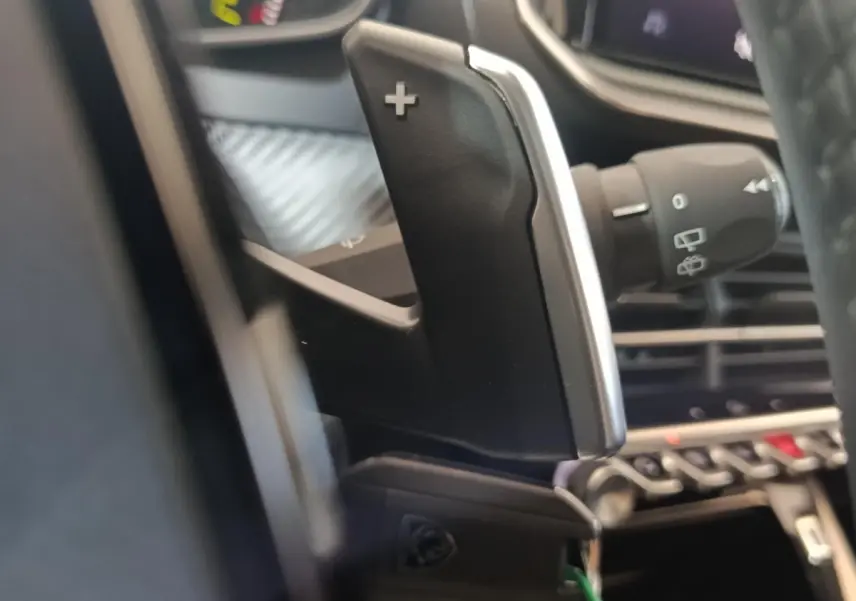 Gros plan sur la palette de changement de vitesse côté droit dans l'habitacle d'une Peugeot 208 gris clair hybride 2025.