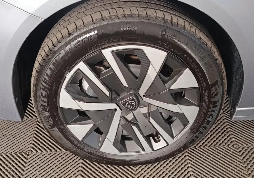 Gros plan sur la roue avant gauche grise d'une Peugeot 208 Hybrid 100 e-DCS6 Style avec jante au design géométrique.