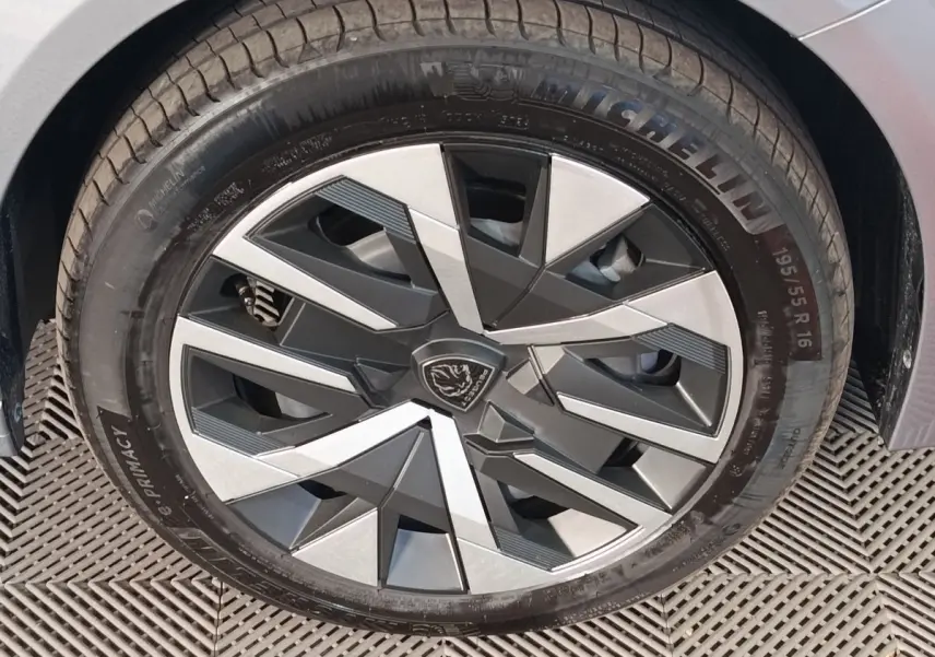 Gros plan sur la roue avant droite gris clair d’une Peugeot 208 Hybrid avec jante au design géométrique noir et argent.
