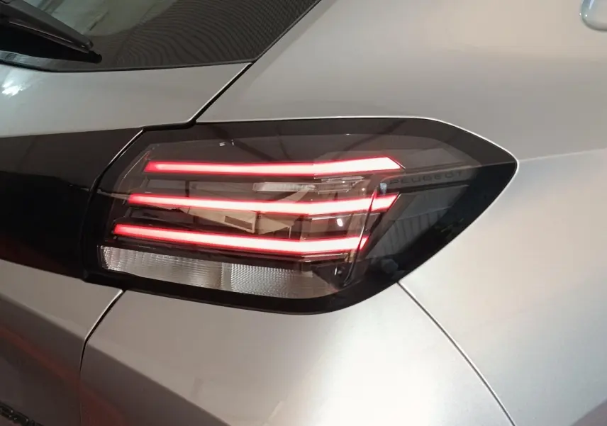 Gros plan sur le feu arrière droit allumé d'une Peugeot 208 Hybrid gris clair, soulignant son design moderne et lumineux.