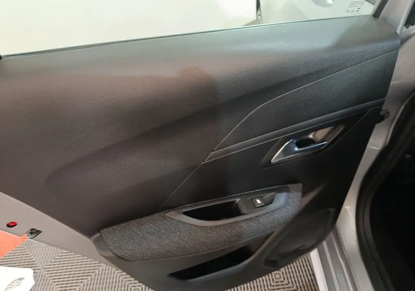 Vue intérieure sur la porte arrière droite d'une Peugeot 208 Hybrid gris clair, avec accoudoir tissu et commande de vitre.