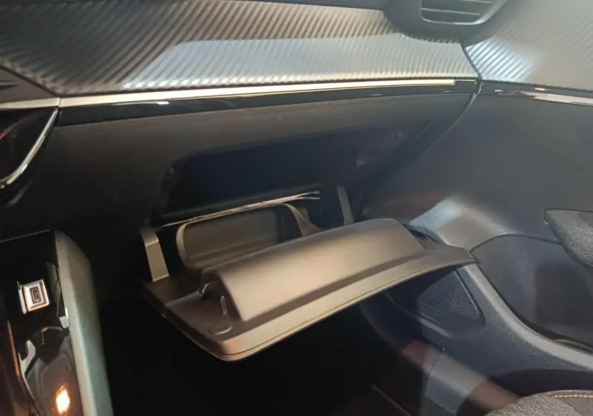 Gros plan sur la boîte à gants ouverte de la Peugeot 208 Hybrid gris clair, montrant le tableau de bord et les finitions intérieures.