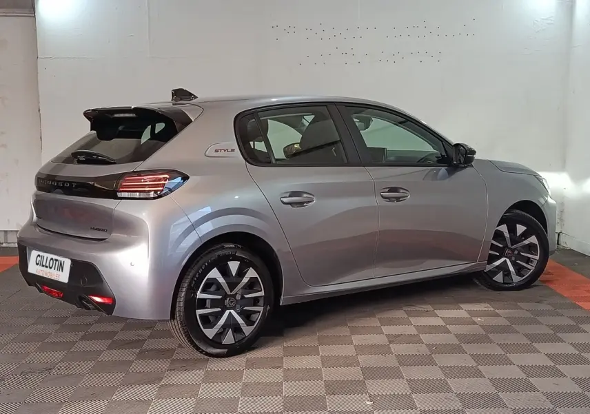 Vue 3/4 arrière droite d’une Peugeot 208 Hybrid gris clair avec jantes noires et badge Style sur l’aile arrière.