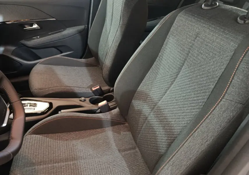 Vue intérieure rapprochée des sièges avant gris foncé avec surpiqûres orange du Peugeot 208 Hybrid 100 e-DCS6 Style 2025.