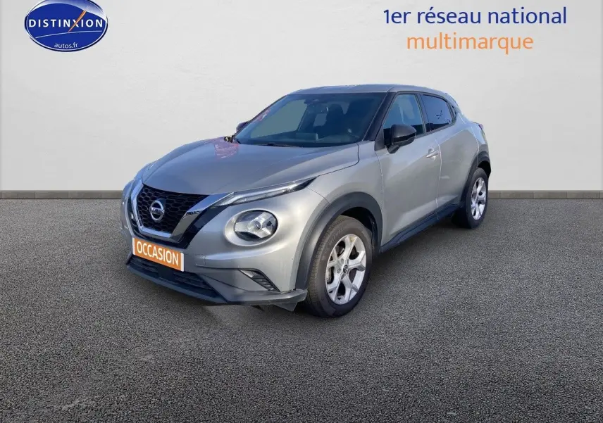 Nissan Juke gris clair vu en 3/4 avant droit, mettant en valeur ses phares ronds et sa calandre noire distinctive.