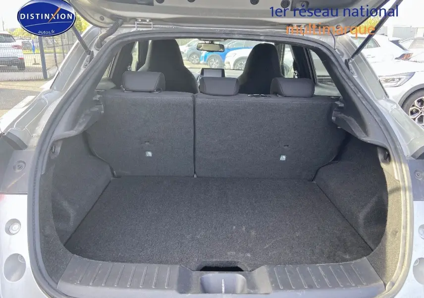Vue arrière du coffre ouvert d'un Nissan Juke gris clair 2021, montrant l'espace de chargement et les dossiers de sièges arrière relevés.