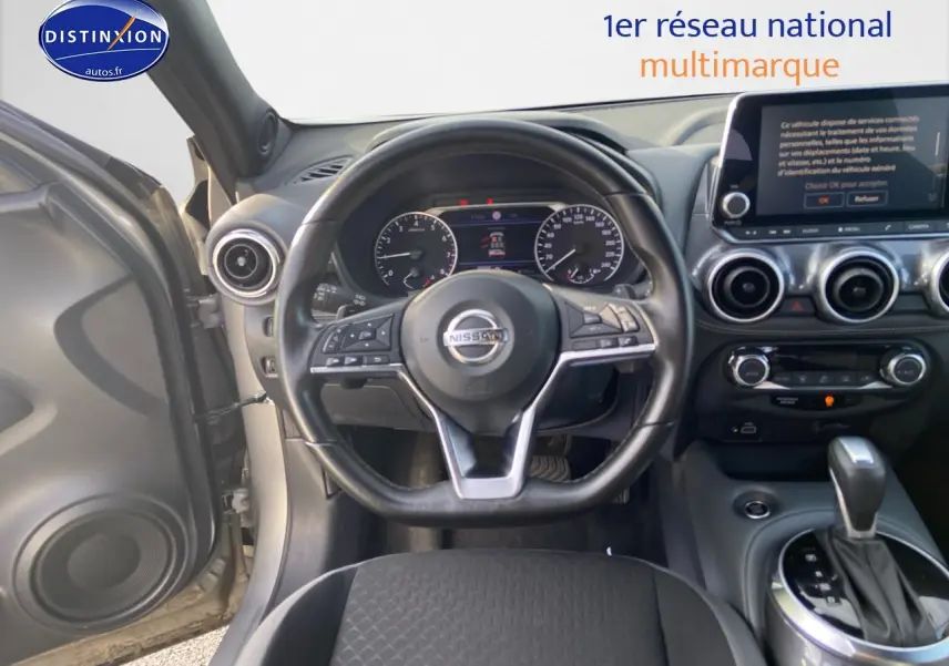 Vue intérieure centrée sur le volant et le tableau de bord d'un Nissan Juke gris clair avec boîte automatique.