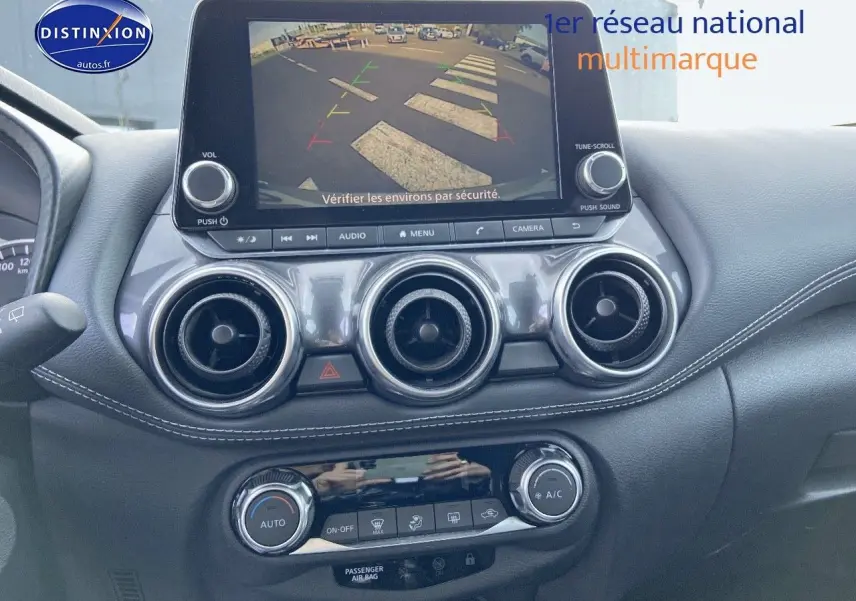 Tableau de bord du Nissan Juke gris clair 2021 avec écran de caméra de recul et commandes de climatisation visibles.