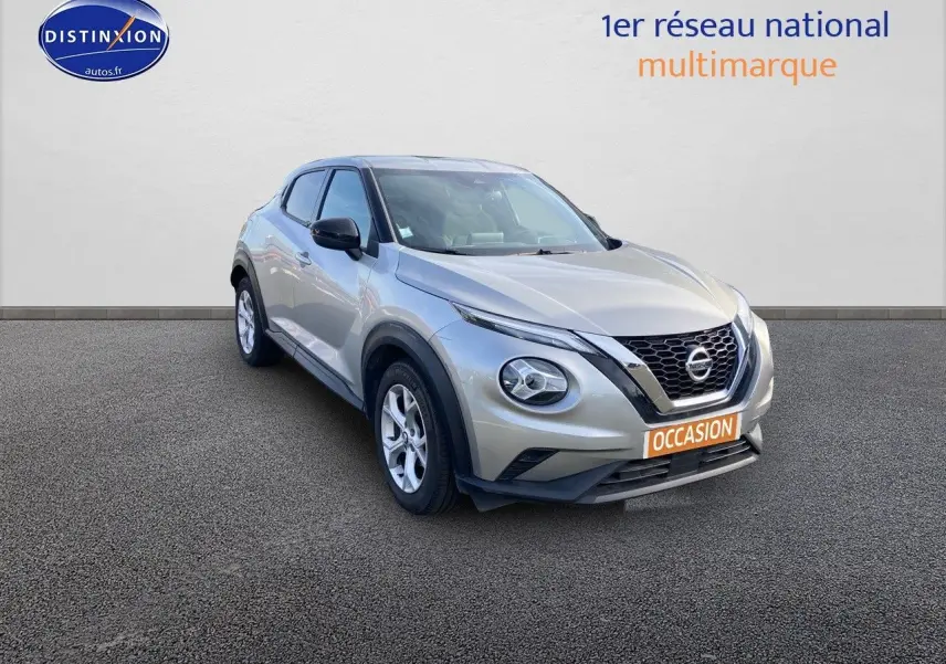 Nissan Juke gris clair vu de 3/4 avant droit avec calandre noire et feux ronds distinctifs.