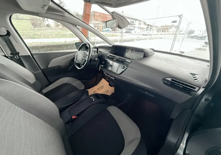 Vue intérieure côté conducteur de la Citroën C4 Picasso gris platinium, montrant tableau de bord et sièges bicolores noirs et gris.