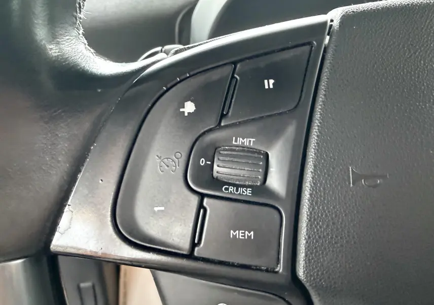 Gros plan sur les commandes de régulateur de vitesse à gauche du volant d’un Citroën C4 Picasso gris platinium.