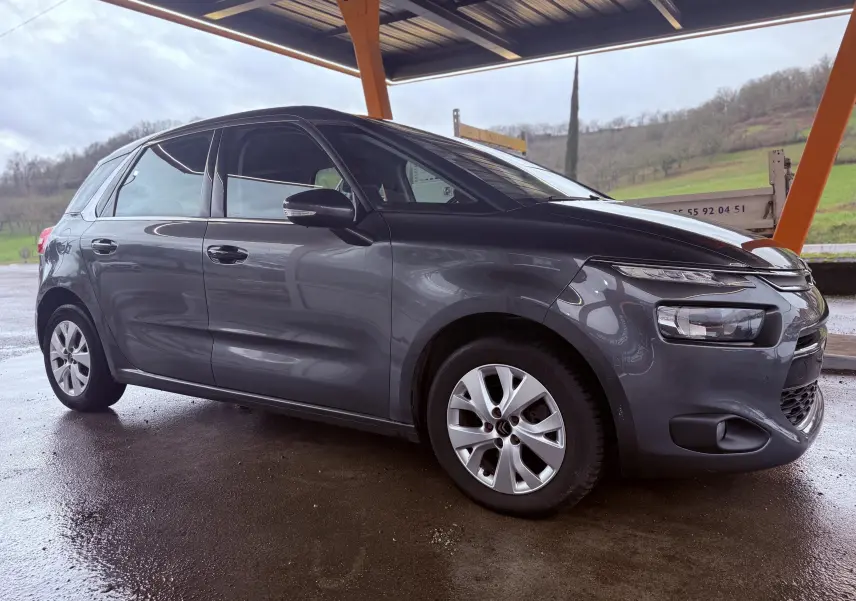 Vue 3/4 avant droit d'une Citroën C4 Picasso gris platinium métallisé sous abri, avec jantes alliage et feux avant distinctifs.