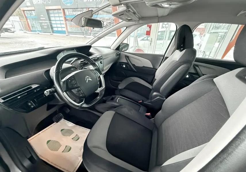 Vue intérieure côté conducteur de la Citroën C4 Picasso 2015, montrant sièges tissu noir et gris et tableau de bord moderne.