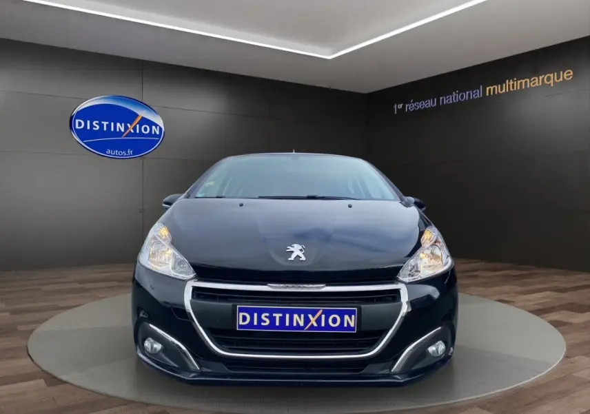 Vue frontale d'une Peugeot 208 AFFAIRE noire, avec phares allumés et calandre chromée dans un showroom.