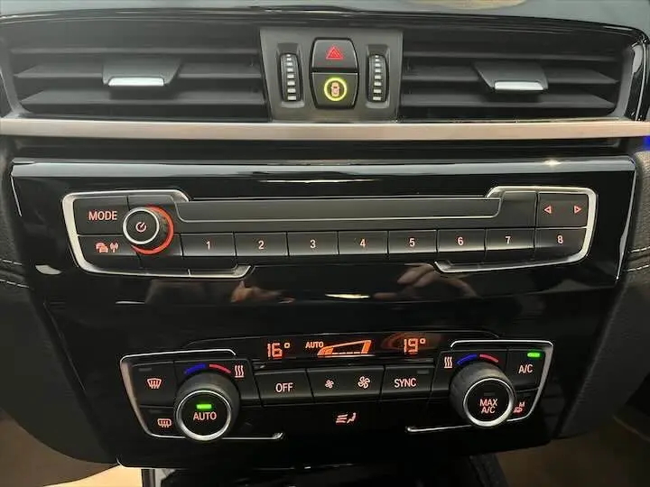 Tableau de bord noir brillant du BMW X2 sDrive 18i 2022 avec commandes climatisation et boutons radio éclairés en orange