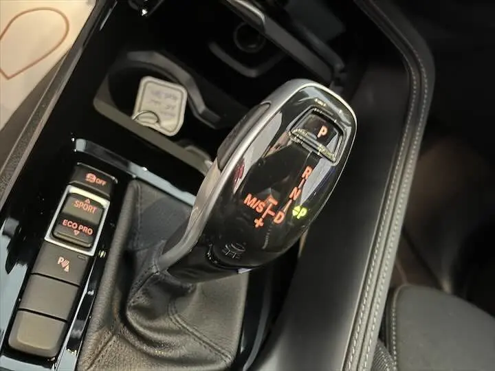 Gros plan sur le levier de vitesse automatique noir brillant du BMW X2 sDrive 18i, entouré de commandes de mode de conduite.