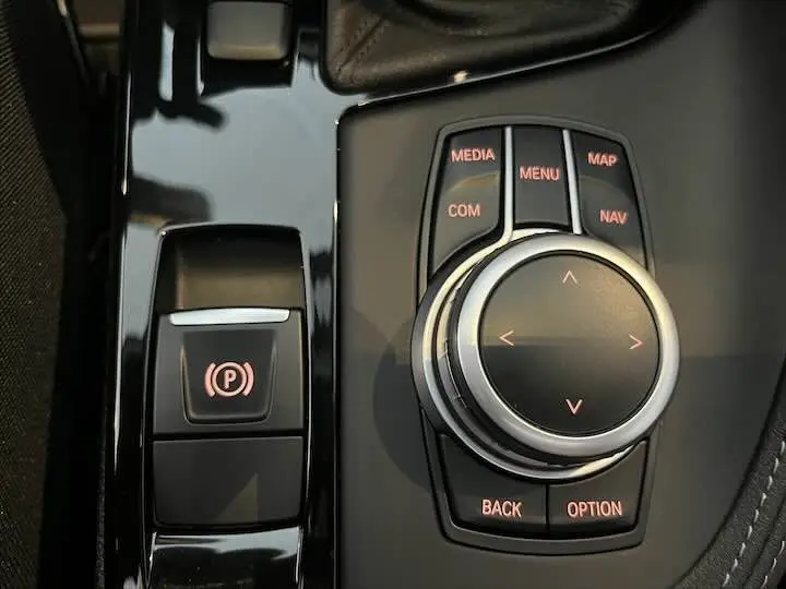 Gros plan sur la molette de commande multimédia et frein à main électrique du BMW X2 noir métal, intérieur moderne.
