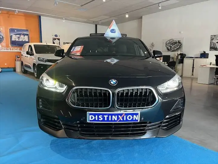 Vue frontale d'un BMW X2 noir métal avec phares allumés et plaque Distinxion en concession.