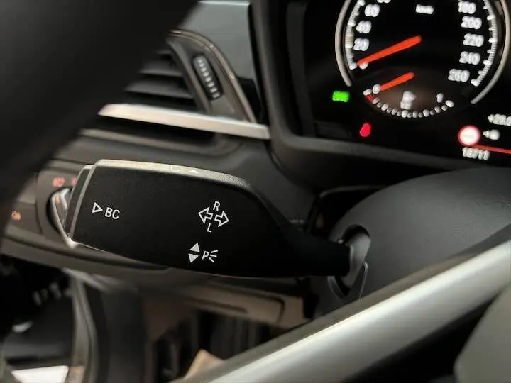 Gros plan sur la commande de clignotant à gauche du tableau de bord d'une BMW X2 noire métal, détails du compteur visibles.