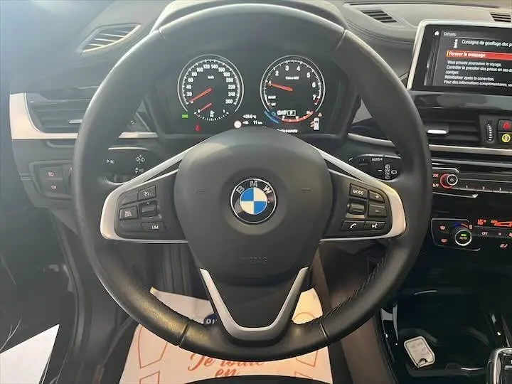 Vue centrée sur le volant noir du BMW X2 2021 avec tableau de bord et écran multimédia allumés.