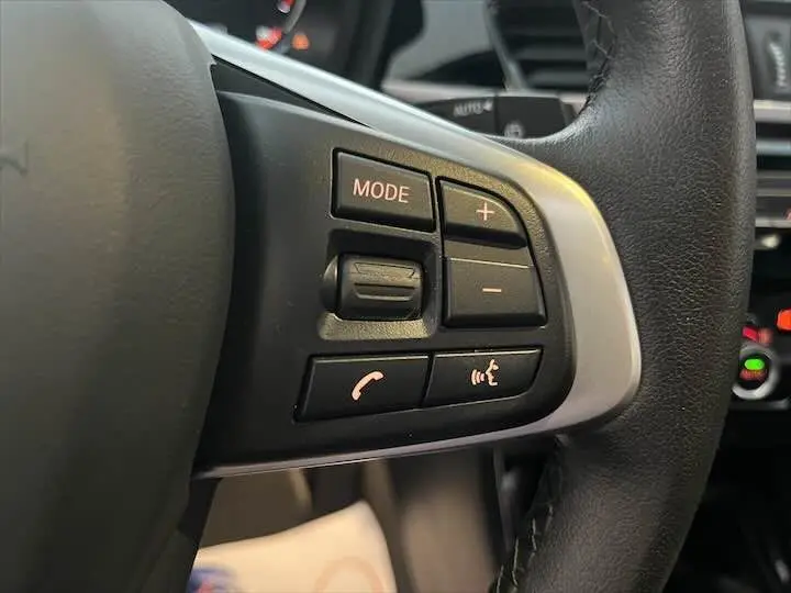 Gros plan sur les commandes multifonctions noires à gauche du volant cuir d'une BMW X2 noire métal, modèle 2022.