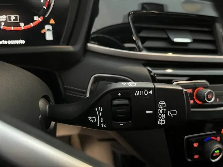 Gros plan sur la commande de l'essuie-glace automatique dans l'habitacle d'une BMW X2 noir métal, tableau de bord en arrière-plan.