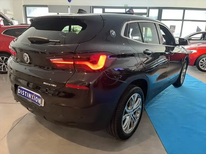 BMW X2 sDrive 18i noir métal vue 3/4 arrière droit avec feux arrière allumés en showroom intérieur