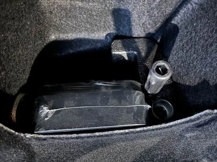 Gros plan sur un compartiment de coffre avec un outil de démontage de roue dans une BMW X2 noir métal.