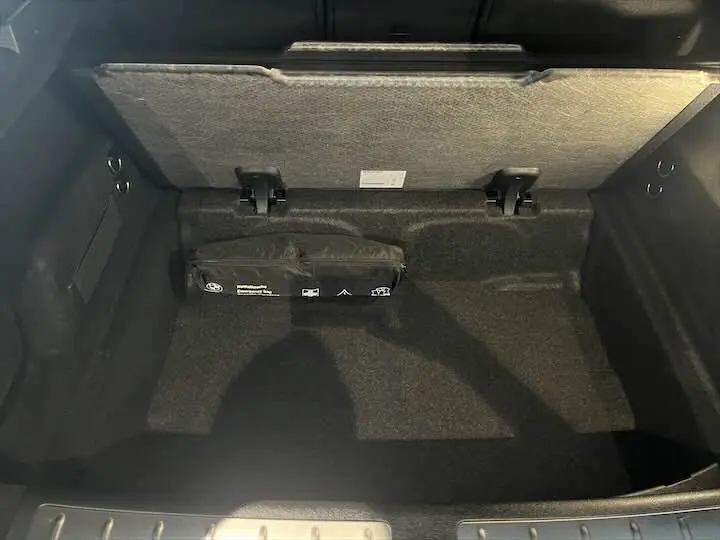 Coffre ouvert d’un BMW X2 noir métal, vue plongeante montrant un rangement avec trousse de secours fixée au fond.