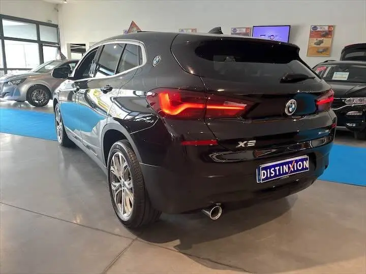 Vue 3/4 arrière droite d'un BMW X2 noir métal avec feux arrière allumés dans un showroom.