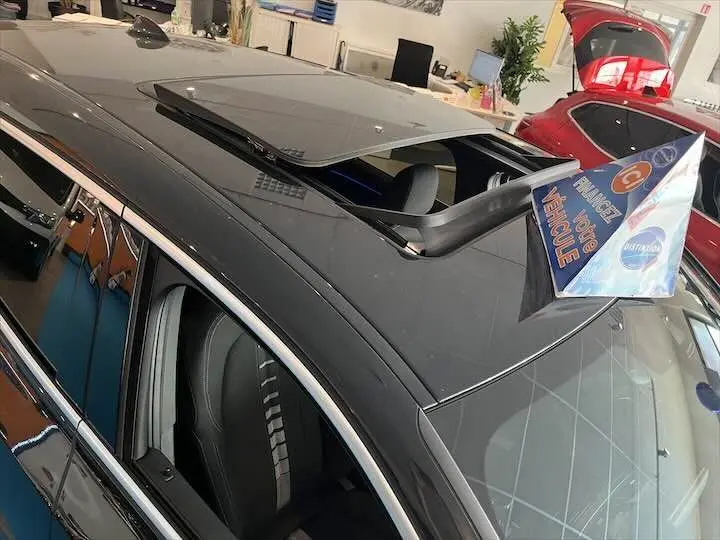 Vue plongeante sur le toit ouvrant ouvert d'un BMW X2 noir métal, avec intérieur et sièges visibles côté gauche.