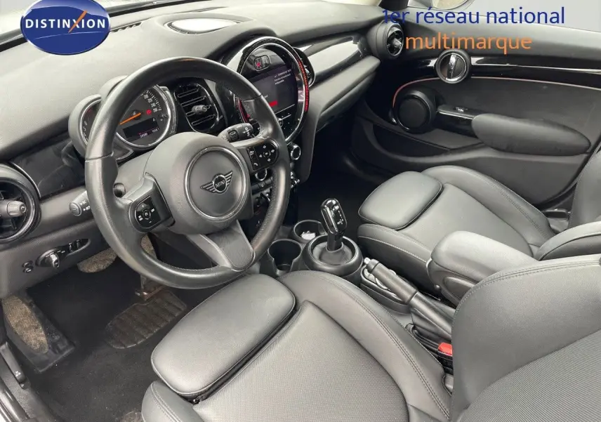 Vue intérieure côté conducteur de la MINI 1.5 136CH STEPTRONIC 2023 avec sièges cuir noir et tableau de bord moderne.