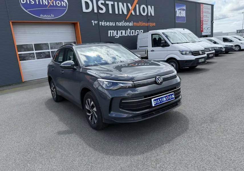 Volkswagen Tiguan 1.5 eHybrid gris dauphin vu en 3/4 avant sur parking devant un bâtiment Distinxion.