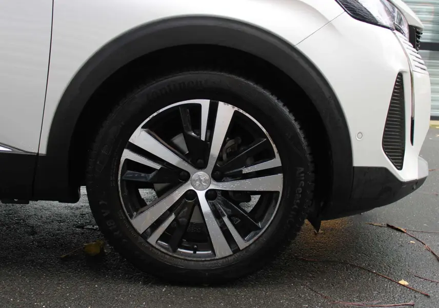 Gros plan sur la roue avant gauche du Peugeot 3008 blanc nacré avec jante alliage bicolore et partie avant du véhicule visible.