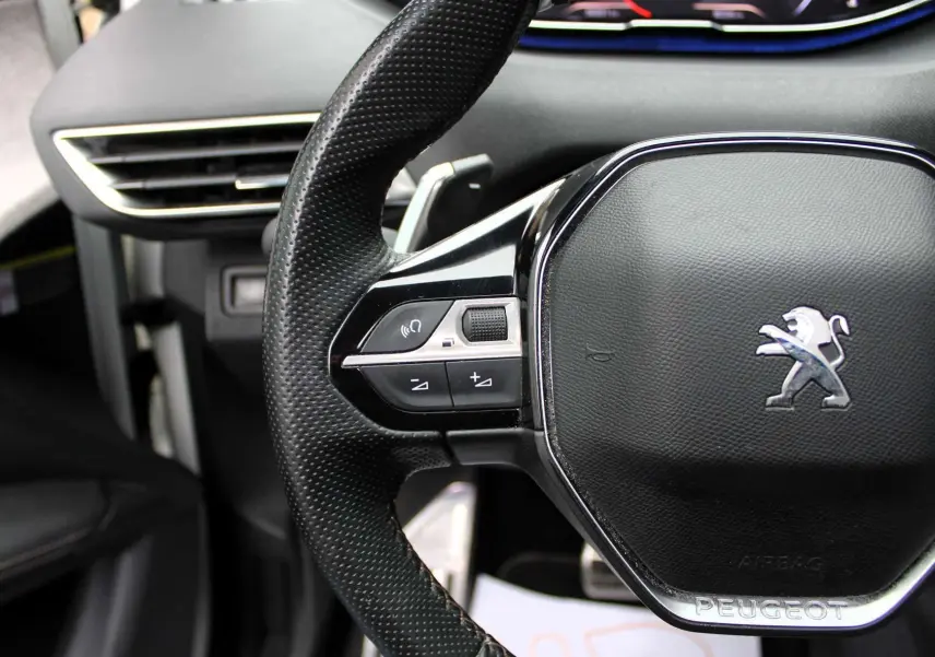 Gros plan sur le volant noir perforé du Peugeot 3008 2025 avec commandes intégrées et logo lion chromé.