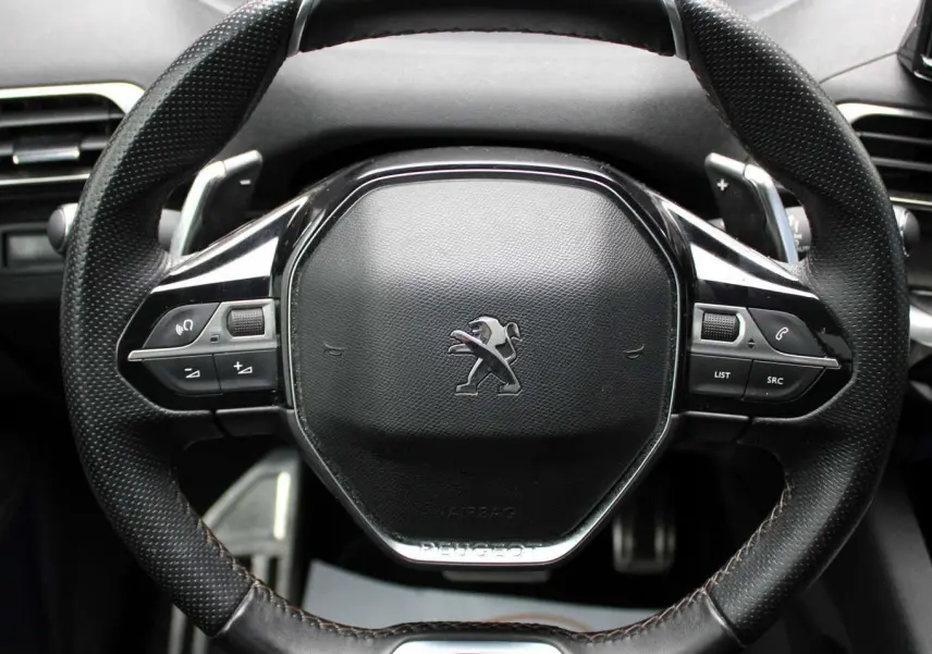 Gros plan sur le volant cuir noir du Peugeot 3008 GT 2025 avec logo lion et badge GT en bas.