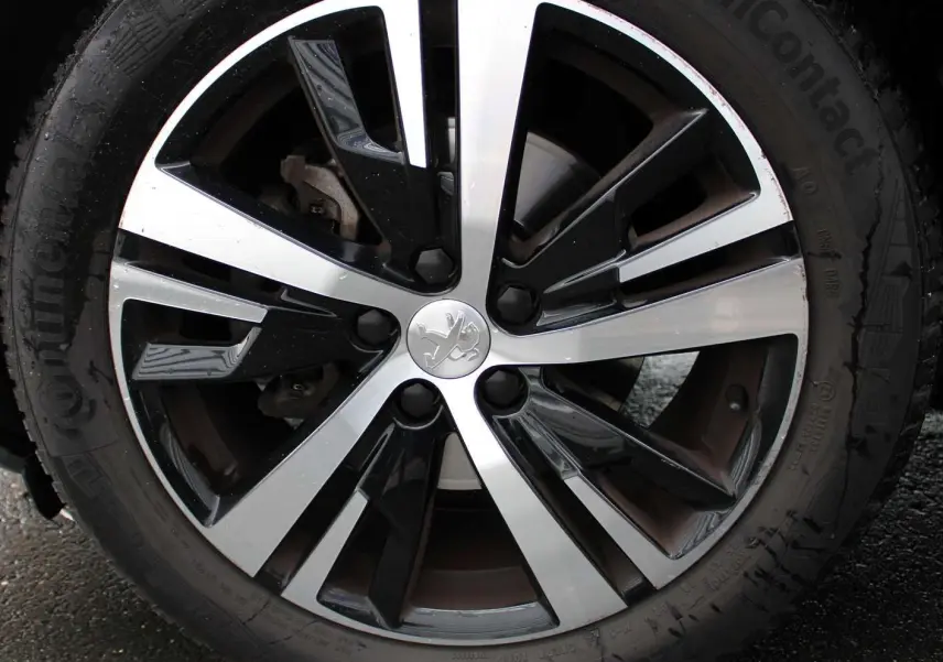 Gros plan sur la jante alliage bicolore noire et argentée avec logo lion Peugeot du 3008 blanc nacré 2025.